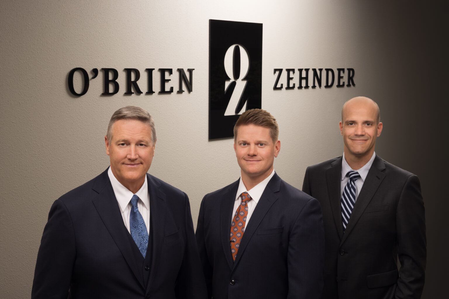 Three O’Brien & Zehnder attorneys standing in front of the firm’s office sign
